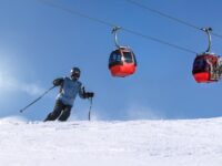 Skier in motion, blue sky, red gondolas, pristine snow, winter sports adventure.