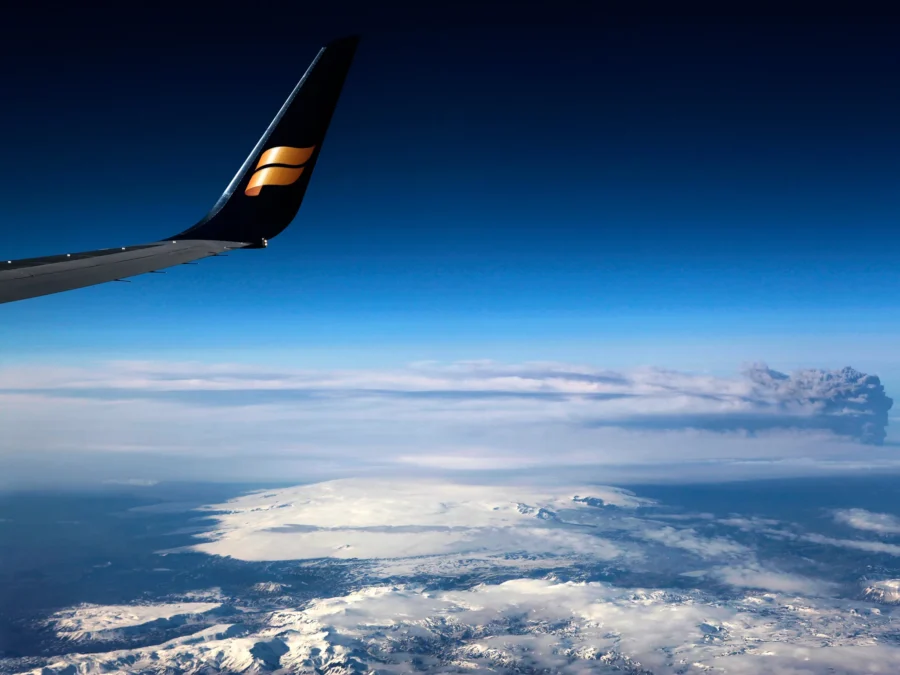 Aerial view: Icelandair flight wing, snow-capped mountains, glacier, dramatic sky.