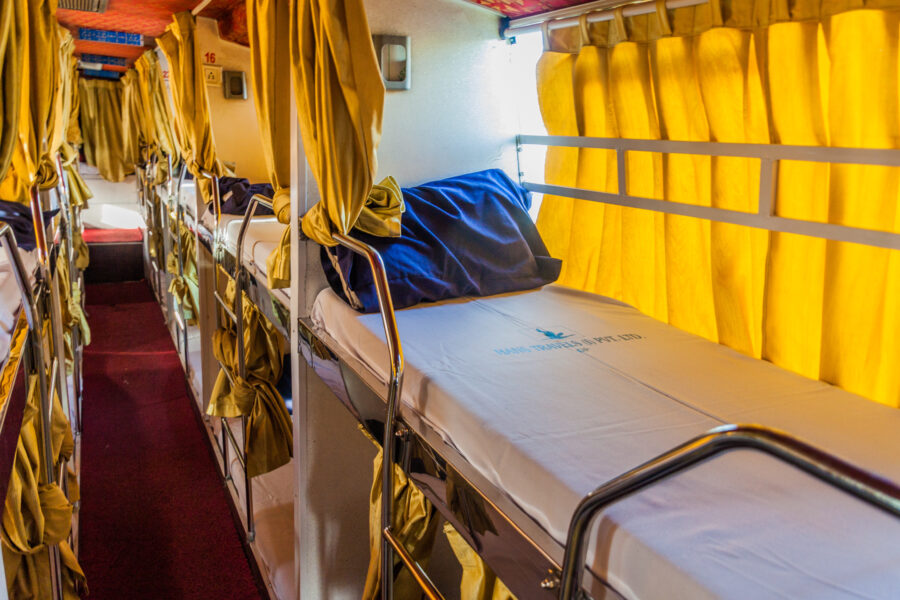 Interior view of a sleeper bus featuring cozy bunks, soft lighting, and spacious seating for comfortable overnight travel.