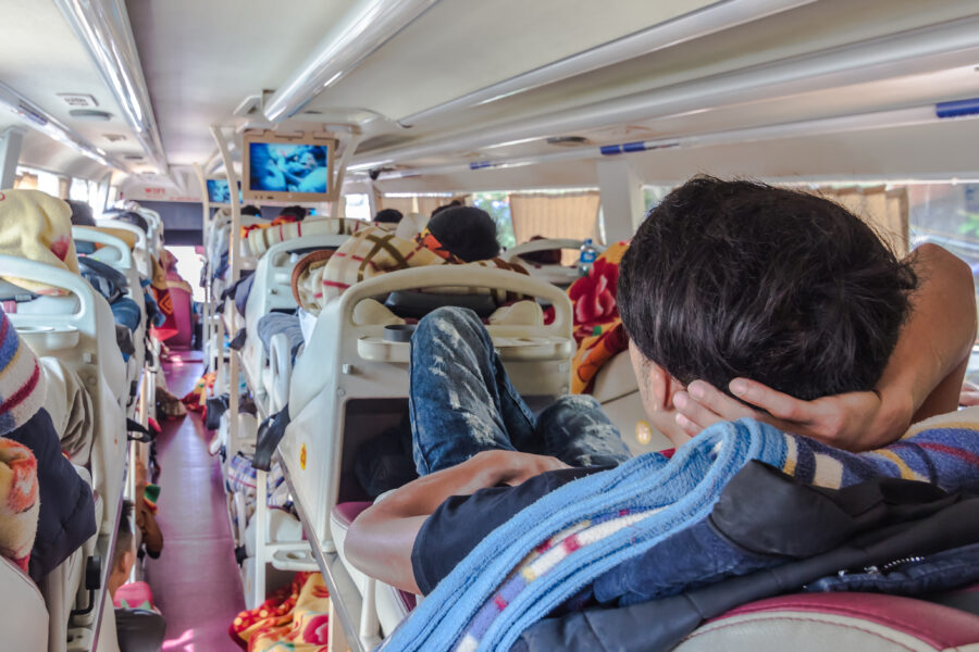 Passengers on a long-distance sleeper bus watching a TV screen, enjoying entertainment during their journey.