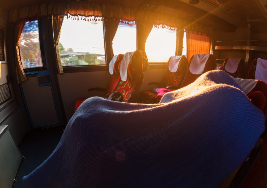 Man relaxing on a sleeping bus, traveling through Thailand's scenic landscapes on a long road trip.