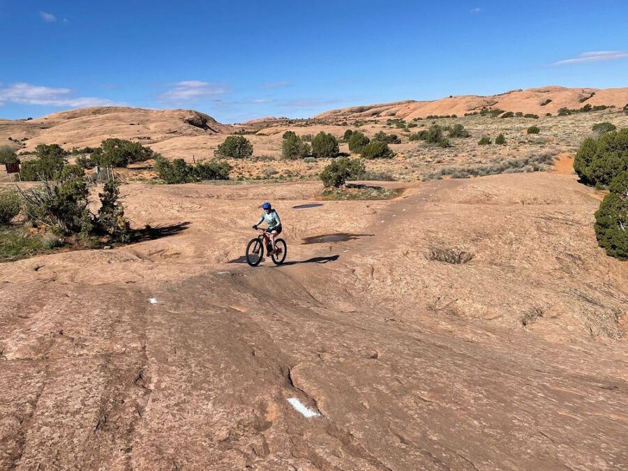 Person rides a mountain bike along the rocky Slickrock Bike Trail, surrounded by rugged terrain and natural beauty.
