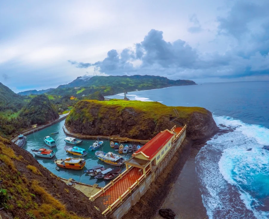 Batanes small harbor with boats, cliffs, and rugged coastline under cloudy sky.