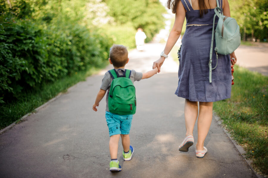 Back view of a mother and her young child, both carrying backpacks, walking together down a pathway