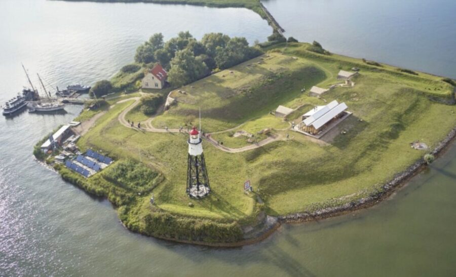 Aerial view of small lighthouse island with boats, harbor, solar panels and historic grassy fortifications.