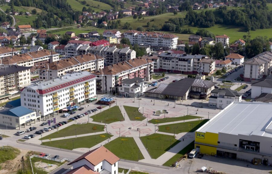 Aerial view of East Sarajevo town square, modern supermarket, residential buildings and surrounding green hills.
