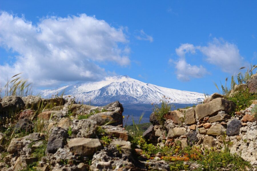 Snow-capped volcanic mountain with ancient ruins and lush greenery under a vibrant blue sky.