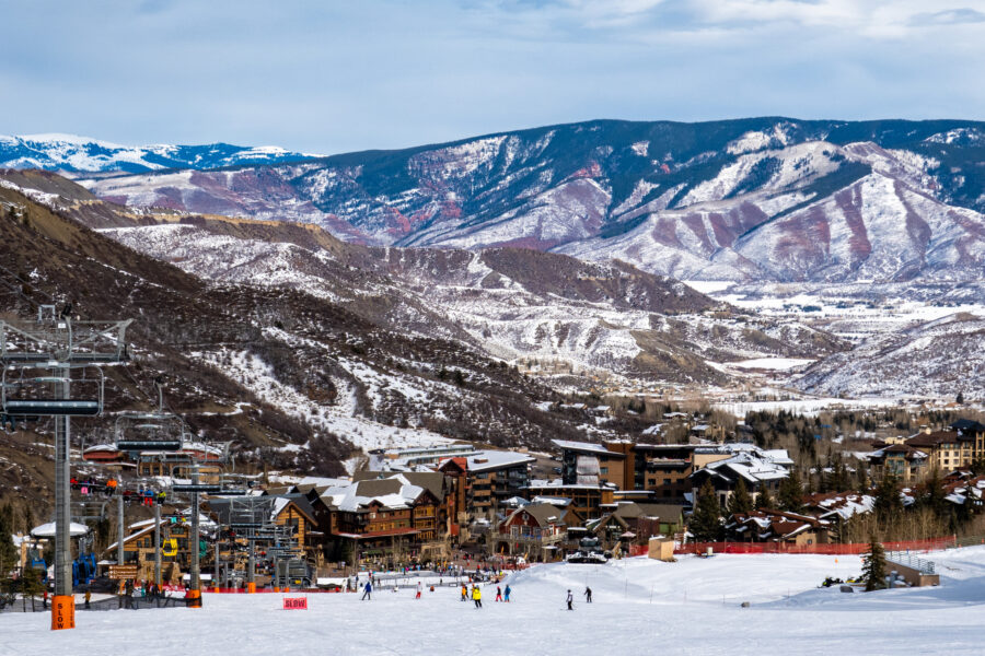 Panoramic view of Snowmass Village with skiers in the foreground and the Rocky Mountains in the background