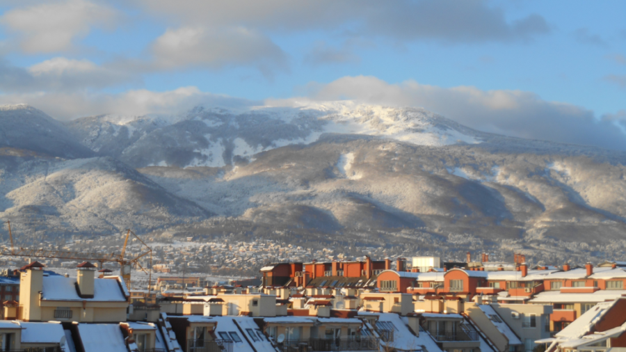 Winter city skyline with snowy rooftops and majestic mountain backdrop.