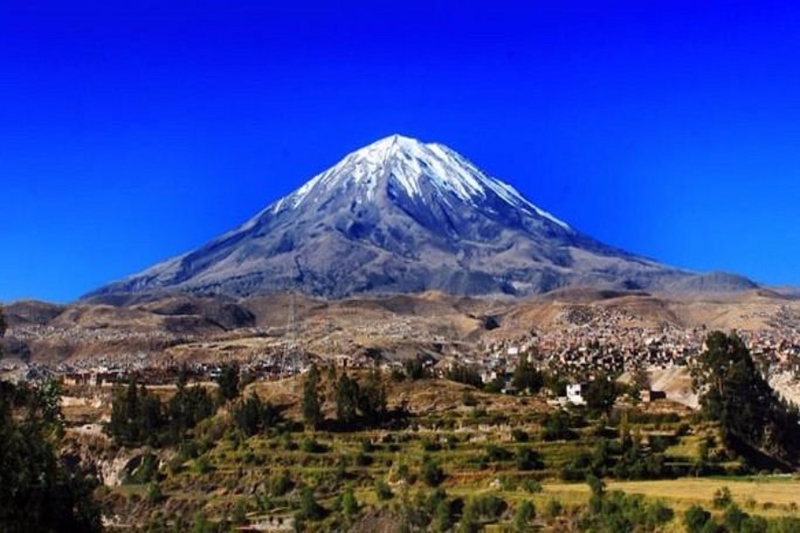 Snow-capped Misti Volcano above Arequipa valley town with terraced farmland and clear blue sky.