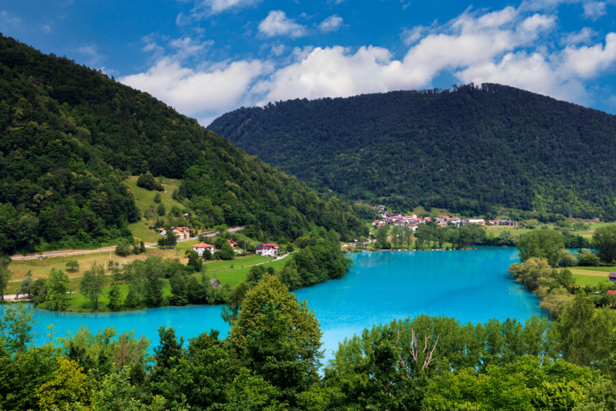 Scenic view of the Julian Alps surrounding Lake Soča in Slovenia, showcasing lush greenery and tranquil waters