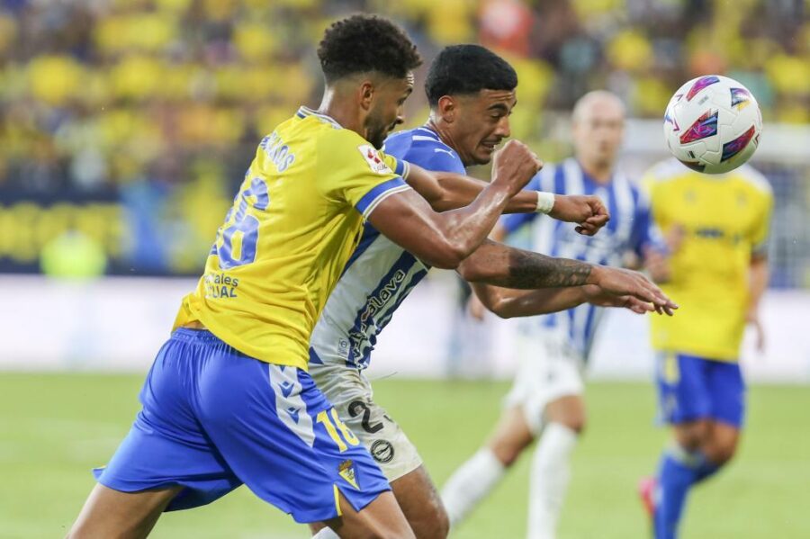 LaLiga soccer aerial challenge: yellow jersey vs striped, players contesting airborne ball.