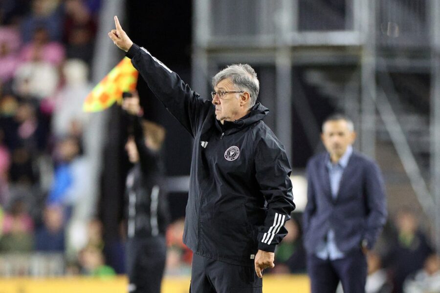 Tata Martino signals strategy to team during intense match with linesman nearby.