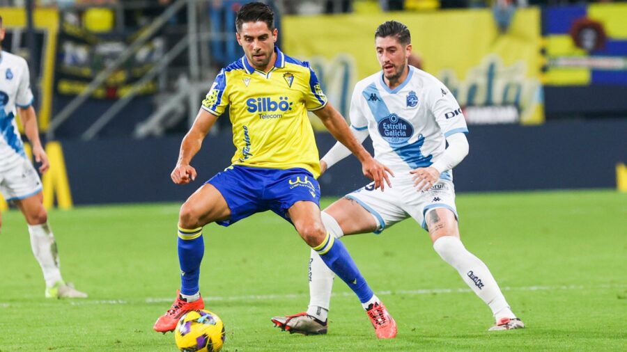 Cádiz vs A Coruña soccer duel: yellow player shielding ball from white opponent.