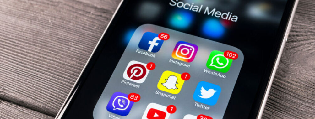 Close-up of a phone on a wooden surface showing icons for Facebook, Instagram, Twitter, and Snapchat social media apps