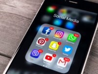 Close-up of a phone on a wooden surface showing icons for Facebook, Instagram, Twitter, and Snapchat social media apps