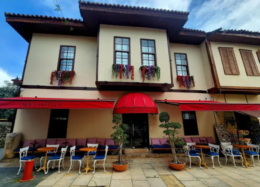 Boutique Antalya hotel with streetfront café, red awnings, flower boxes, and outdoor seating.