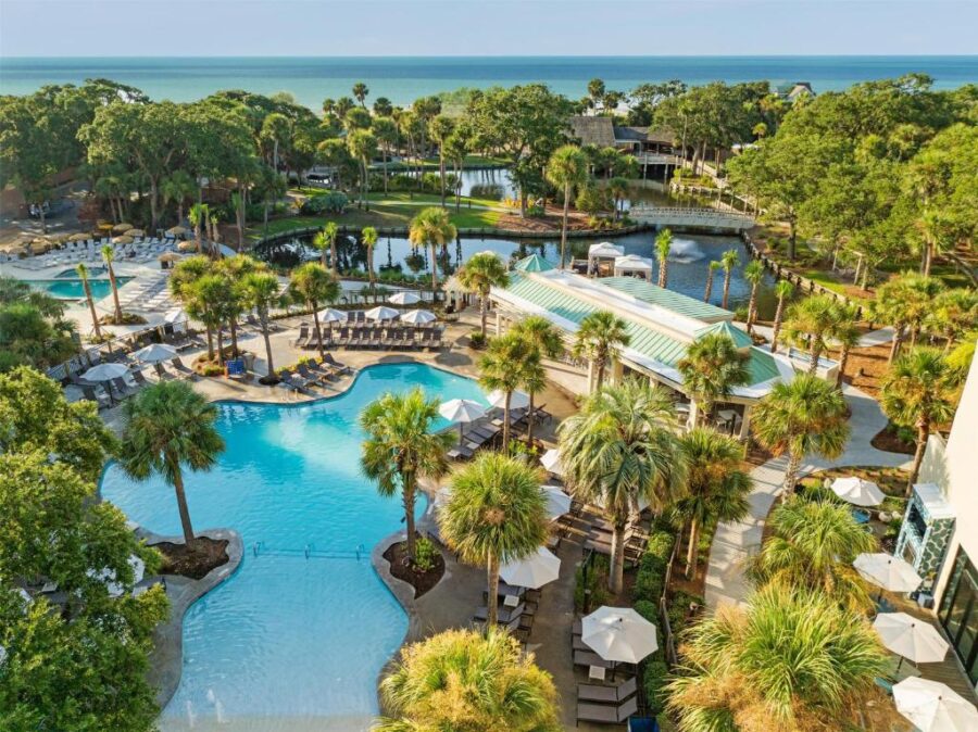 Scenic view of the pool and beach at Sonesta Resort Hilton Head, featuring lounge chairs and tropical landscaping.