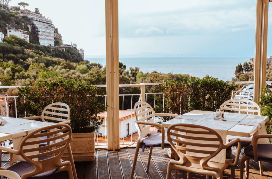 Panoramic Sorrento sea view from a terrace featuring vacant tables and stylish beige seating