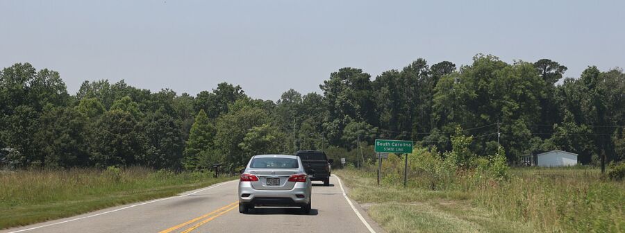 Rural road near South Carolina border with cars, greenery, and directional sign.