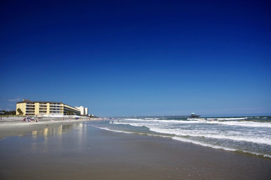 Tranquil scene at Folly Beach, South Carolina, featuring a few individuals walking along the sandy beach by the water