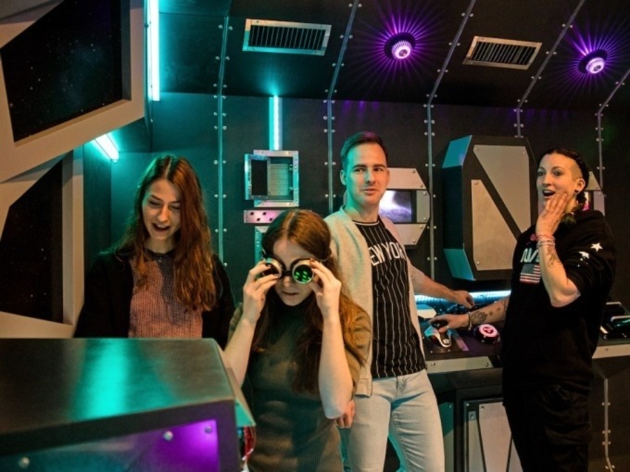Three people stand in front of a video game machine at TeamEscape SPACE ESCAPE in Ulm, engaged and ready to play.
