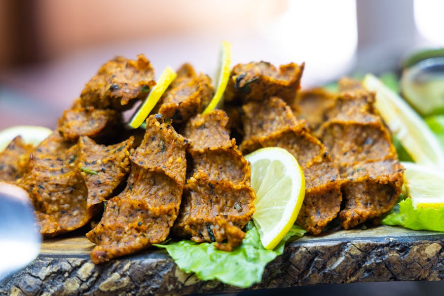 Spiced herbed finger patties on rustic wooden board with lemon wedges and lettuce appetizer.