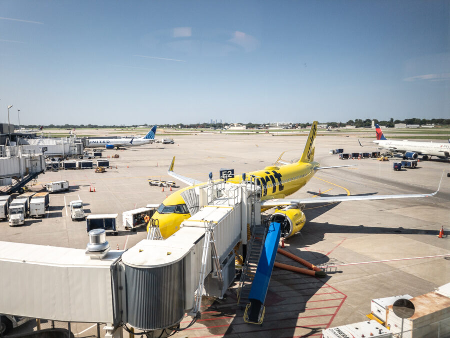 Spirit Airlines Airbus A320 in yellow boards at Minneapolis–Saint Paul International Airport, with Delta and United aircraft on the tarmac.