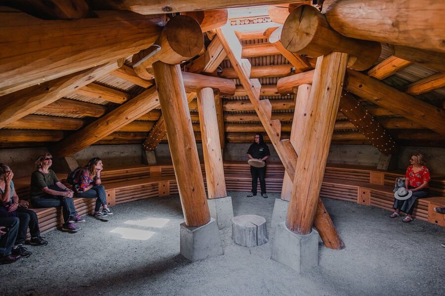 People seated in a room with wooden beams and a bench at the Squamish Lil’wat Cultural Centre in Whistler, Canada.