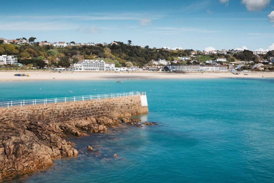 Scenic beach in St. Brelade, Jersey, featuring a pier and charming houses along the shoreline.