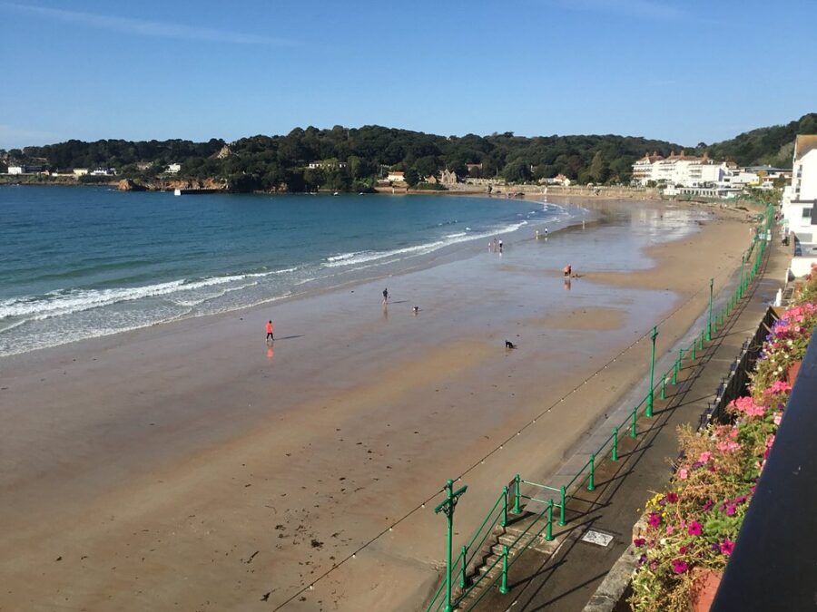 Balcony view of St. Brelade’s Bay Beach, featuring golden sand and tranquil waves under a clear sky.