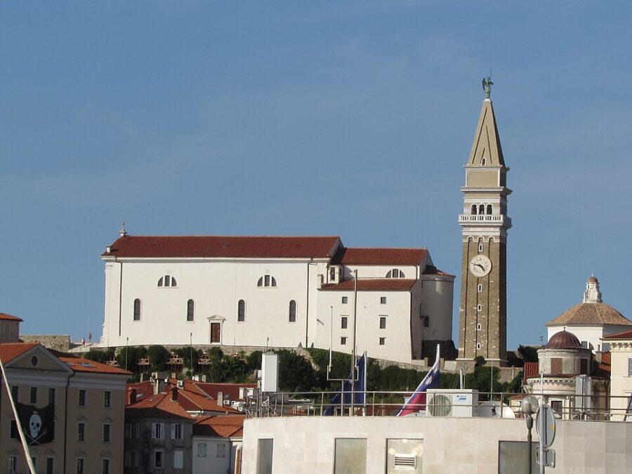 St. George Church in Piran, Slovenia, showcasing a clock tower and a boat in the foreground.