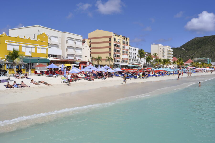 Visitors enjoy sunbathing on the sandy beach of St. Maarten, with vibrant blue water and lush palm trees nearby 