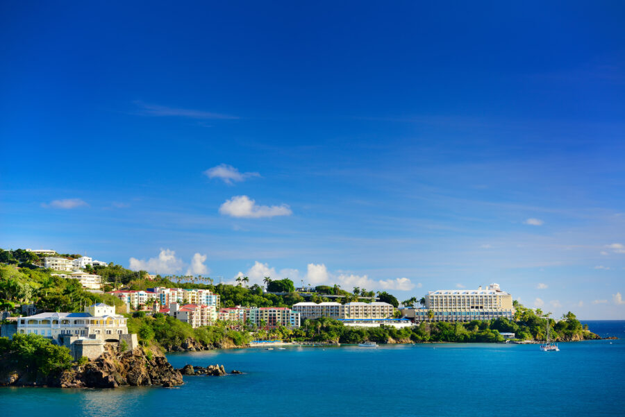 Scenic panorama of St. Thomas harbor, featuring sailboats and lush green hills against a bright blue sky.