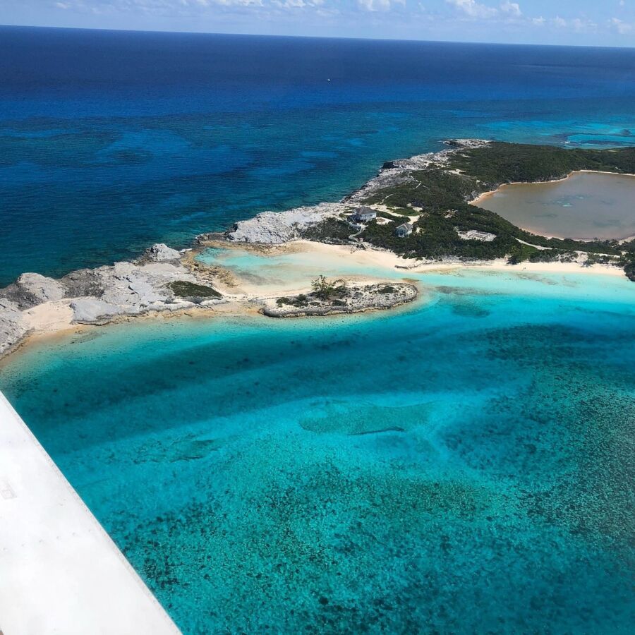 Turquoise waters of Staniel Cay, Bahamas, shimmering under the sun, surrounded by lush greenery and rocky shores.