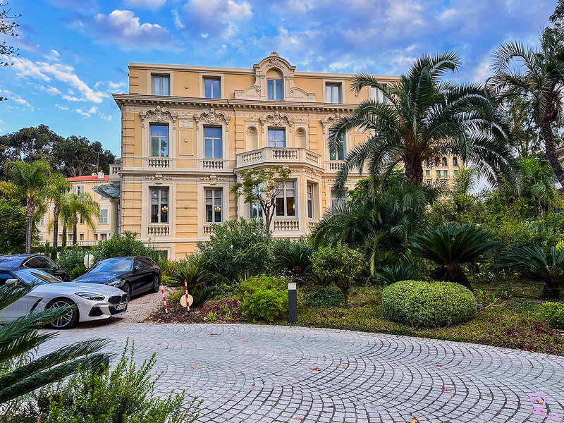 Historic Menton yellow villa hotel with palm garden and cobblestone driveway.