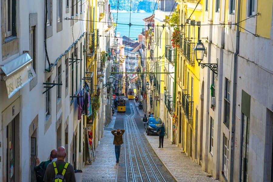 Bairro Alto Lisbon tram street on cobblestones with yellow buildings and sea view.