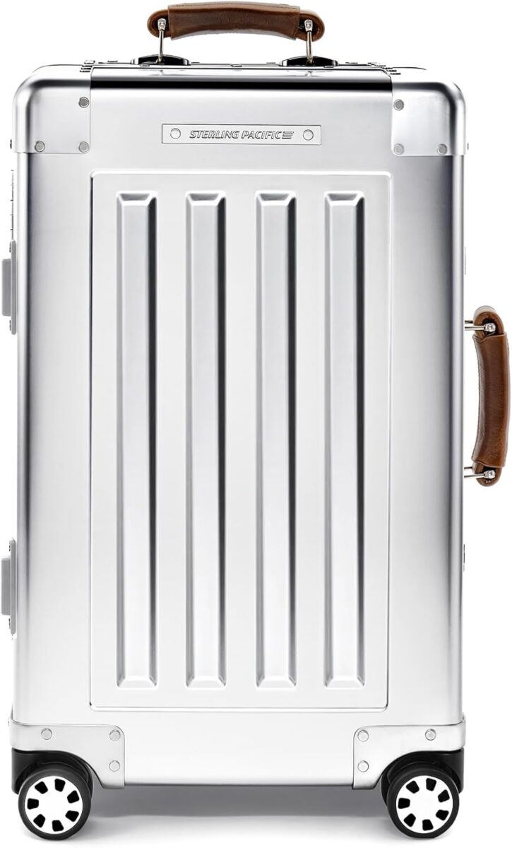 Sterling Pacific 40L Cabin Travel Case chrome-colored, hard-shell suitcase with vertical grooves and brown leather handles. It features four black-and-white wheels, exuding a sleek, modern vibe.