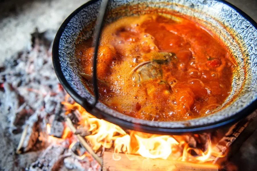 Fishermans tomato soup (halászlé) simmering in an enamel pot over an open wood fire.