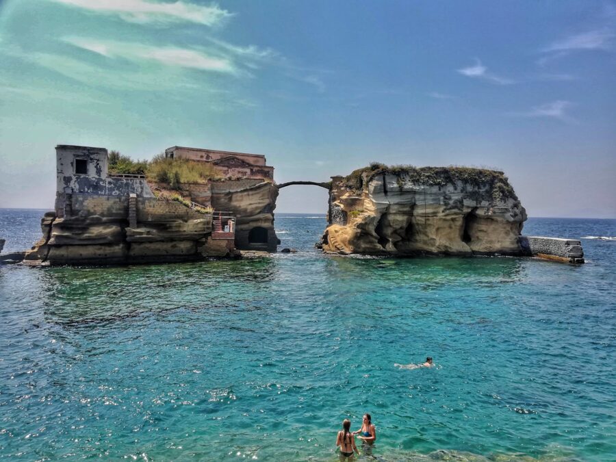 Gaiola Beach stone arch islets with ruined house and turquoise Mediterranean waters.