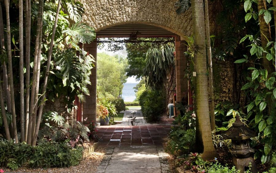 Stone archway garden path lined with tropical plants leading to seaside view.