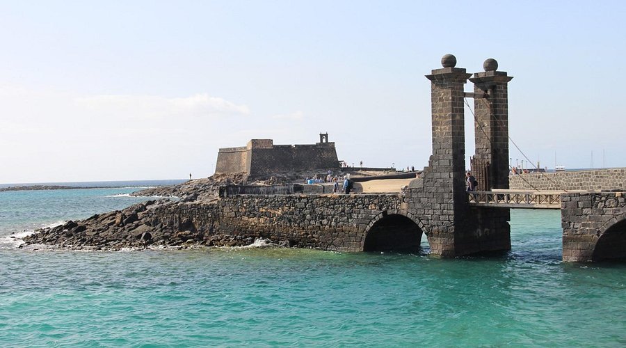 Historic stone bridge and coastal fortress over turquoise water in Arrecife, Lanzarote, Canary Islands.