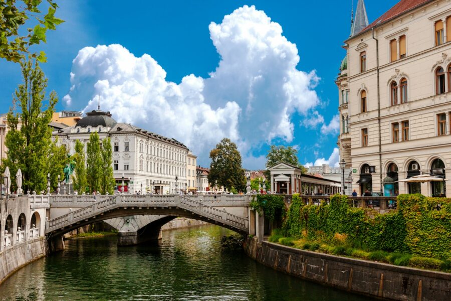 Ljubljana Old Town stone bridge over canal with riverside cafes and historic architecture.