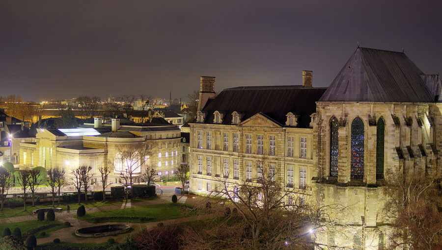 Palace of Tau, Rouen, at night with illuminated stone buildings, formal garden, stained glass windows.