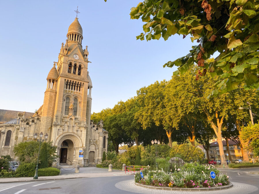 Épernay stone church with bell tower and flowered roundabout at sunset.