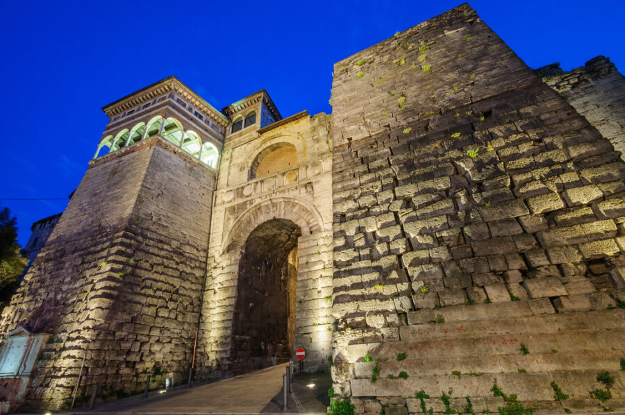Etruscan stone archway at dusk, illuminated ancient city gateway.