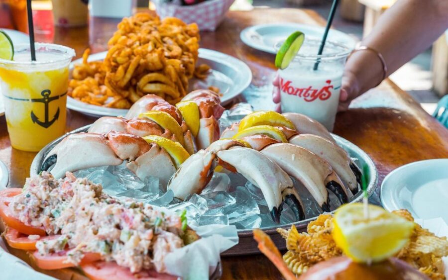 Stone crab claws platter with lobster roll, curly fries, and frozen drinks on rustic table.
