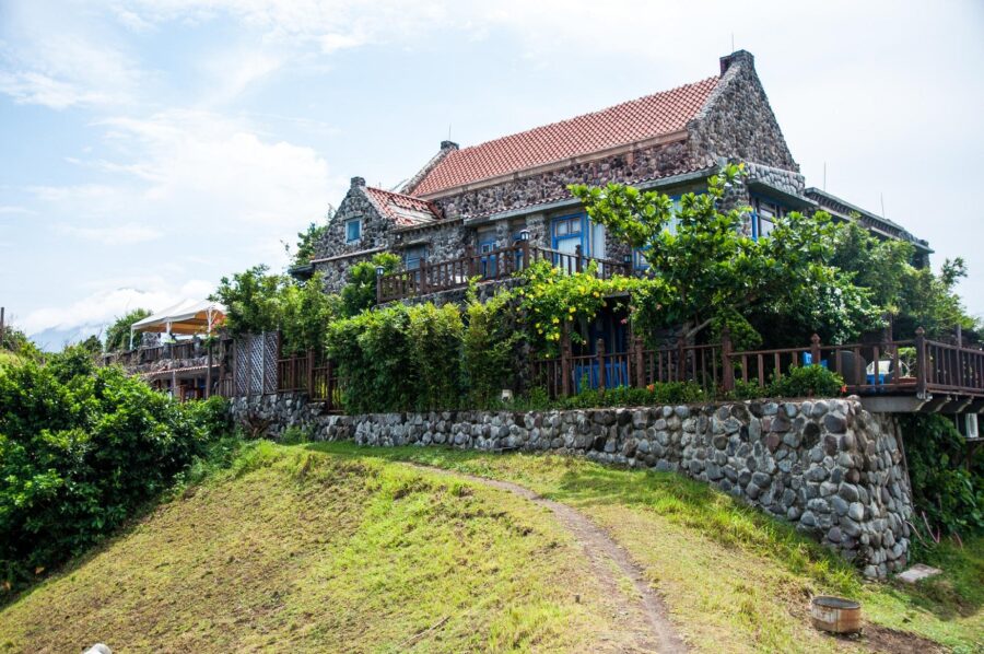 Rustic stone hillside cottage with terracotta roof, wraparound balcony, and lush garden.
