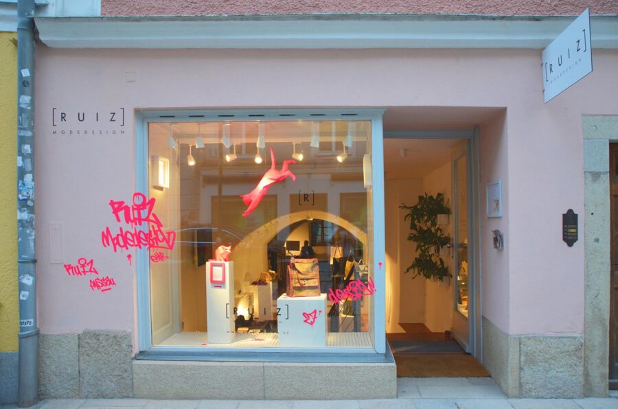 Pink minimalist boutique storefront with suspended fuchsia sculpture and graffiti-tagged display window.