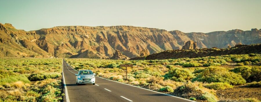 Scenic two-lane highway with silver car driving toward desert cliffs.